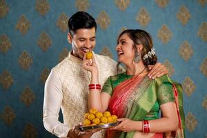 une image de une charmant couple portant traditionnel Indien tenue profiter laddus pendant le diwali Festival photo