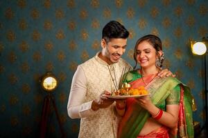 charmant couple dans traditionnel Indien tenue porter une puja thali dans leur mains tandis que permanent dans de face de le caméra photo
