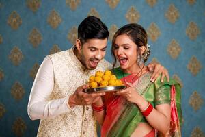 image de romantique couple en riant tandis que en portant assiette de ladoo pendant diwali Festival photo