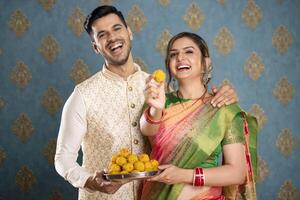 une content mari et épouse pose pour le caméra avec assiette de laddu dans leur mains photo