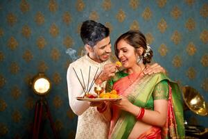 image de une aimant couple dans traditionnel Indien tenue pendant le diwali fête en portant une pooja assiette et souriant tandis que en mangeant ladoos photo