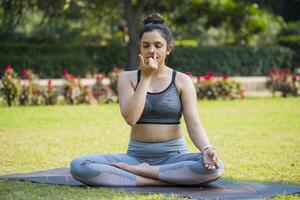 à le parc, un asiatique en forme femme se ferme sa yeux et Faire respiration exercer. photo