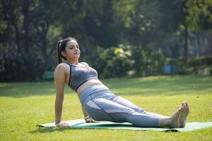 tandis que séance dans le parc, un Indien jolie femme grèves une yoga pose. photo