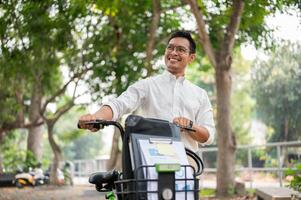 une content, insouciant asiatique homme d'affaire pousser le sien vélo, en marchant dans le Publique parc. photo