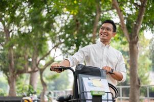 une content, insouciant asiatique homme d'affaire pousser le sien vélo, en marchant dans le Publique parc. photo