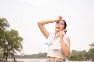 une malaise femme détient une l'eau bouteille tandis que essuyage sa front, permanent en plein air sur une chaud journée. photo