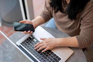 une femme en utilisant sa téléphone intelligent et portable ordinateur, travail à distance à une café magasin. photo