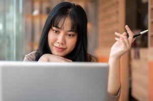 une magnifique asiatique femme est travail à distance à une café, se concentrer sur sa portable ordinateur. photo