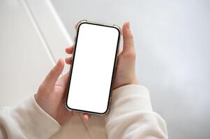 une femme dans une blanc chandail en portant une téléphone intelligent Écran blanc maquette plus de une blanc table à l'intérieur. photo