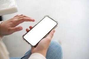 une fermer image de une femme dans jeans est assis intérieur et les usages sa téléphone intelligent. photo