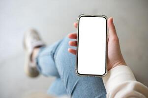 une fermer image de une femme dans jeans est assis intérieur et les usages sa téléphone intelligent. photo