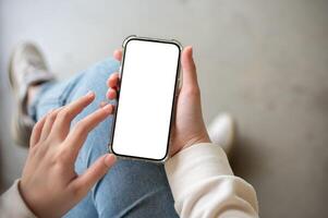 une fermer image de une femme dans jeans est assis intérieur et les usages sa téléphone intelligent. photo