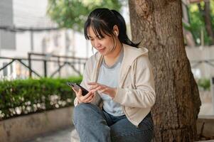 Jeune asiatique femme portant écouteurs, en utilisant sa téléphone, écoute à la musique tandis que effrayant dans une ville parc photo