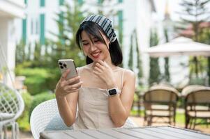 une femme des rires à sa téléphone et jouit bavardage avec sa copains en ligne tandis que relaxant dans une jardin. photo