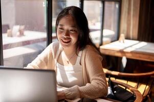 Jeune positif asiatique femme travail à distance à une café boutique, travail sur sa portable ordinateur. photo