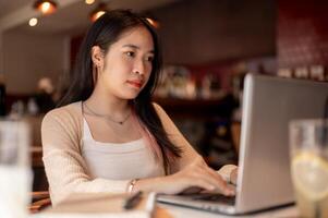 Jeune concentré asiatique femme travail sur sa portable ordinateur tandis que séance dans une café magasin. photo