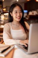 Jeune positif asiatique femme travail à distance à une café boutique, travail sur sa portable ordinateur. photo