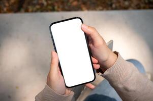 une fermer image de une femme dans jeans est assis en plein air sur une ensoleillé journée et les usages sa téléphone intelligent. photo