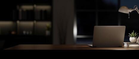 une portable ordinateur sur une table dans une moderne foncé pièce à nuit avec une faible lumière de une table lampe. photo