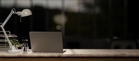 une portable ordinateur sur une marbre table dans une moderne foncé Bureau à nuit. photo