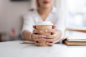 une fermer image de un asiatique femme en portant une à emporter café tasse, séance dans une café magasin. photo