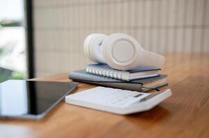 une fermer image de une calculatrice, une tablette, livres, et écouteurs sur une table dans un Bureau chambre. photo