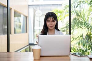 un attrayant asiatique femme d'affaires travail sur sa portable ordinateur dans une café magasin cotravail espace. photo