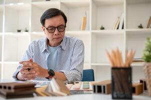 une Sénior asiatique Masculin intérieur designer se concentrer sur travail sur une Nouveau projet dans le bureau. photo