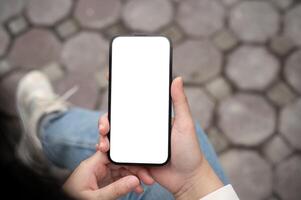 une femme en portant une téléphone intelligent avec une Écran blanc maquette plus de sa tour tandis que séance en plein air. photo