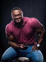 portrait de Beau Jeune africain homme dans court manche chemise séance avec téléphone dans mains sur une chaise. musclé Masculin modèle avec mobile téléphone. fermer. photo