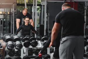 magnifique fille avec mains sur haltères à la recherche sur sa réflexion dans le miroir dans une des sports salle. svelte Jeune femme est prise haltères dans de face de une miroir dans aptitude club photo