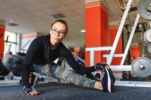 jolie fille Faire élongation des exercices sur le sol à le salle de sport. photo