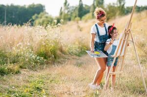 Jeune attrayant mère enseigne fille La peinture dans été parc. en plein air activité pour école âge les enfants concept. photo