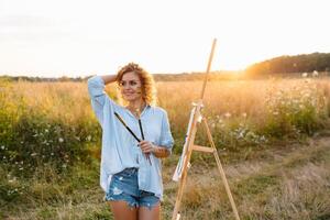 jolie femme est peinture. ouvert air session. mignonne femme dessine une image à le coucher du soleil. fille artiste. photo