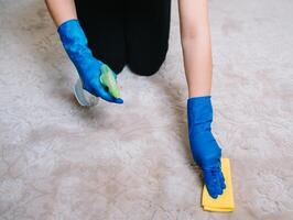 personnes, travaux ménagers et Entretien ménager concept - proche en haut de femme dans caoutchouc gants avec tissu et détergent vaporisateur nettoyage tapis à maison. proche en haut de femme avec tissu nettoyage tapis photo