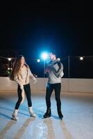 homme et femme Jeune famille content sourit tenir mains patin sur hiver patinoire à nuit, avec bokeh lumières. photo
