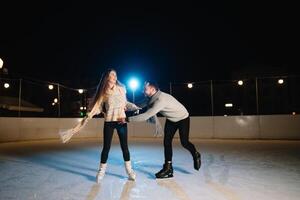 homme et femme Jeune famille content sourit tenir mains patin sur hiver patinoire à nuit, avec bokeh lumières. photo