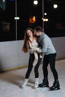 couple sur le ville patinoire dans une hiver soir. gars portion agréable fille à patin sur le la glace dans le foncé nuit et scintille éclairage au dessus leur photo