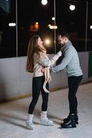 hiver patins, aimant couple en portant mains et roulant sur patinoire. éclairage dans arrière-plan, nuit. concept entraînement. photo