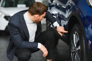 coup de une content homme séance confortablement dans une Nouveau voiture à le concession professionnel vendeur montrant lui quelque chose sur le tableau de bord expliquant voiture les caractéristiques achat voitures. photo