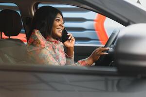 africain américain femme séance dans voiture utilisation mobile téléphone envoyer des SMS tandis que conduite dangereux photo