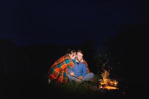 camping nuit dans montagnes. touristique couple séance dans de face de illuminé tente allumé par brûlant feu de camp. tourisme et Extérieur activité concept. photo