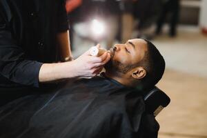 une coiffeur est Aller par le électrique Coupe et rasage machine pour le barbe de un Afro-américain brésilien garçon. photo