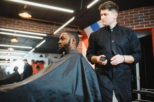 portrait de Jeune noir homme étant taillé avec professionnel électrique tondeuse machine dans salon de coiffure.male beauté traitement concept. Jeune africain gars avoir Nouveau la Coupe de cheveux dans coiffeur salon photo