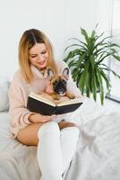 fille en train de lire une livre. mignonne fille en train de lire une livre avec sa chien à maison. jolie élégant fille. photo