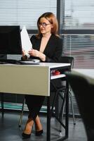 Jeune femme d'affaires séance à lieu de travail et en train de lire papier dans Bureau photo