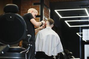 fabrication la Coupe de cheveux Regardez parfait. Jeune barbu homme avoir la Coupe de cheveux par coiffeur tandis que séance dans chaise à salon de coiffure. photo