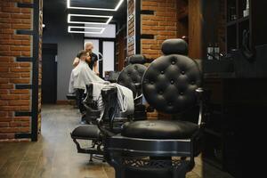 Jeune Beau coiffeur fabrication la Coupe de cheveux de attrayant barbu homme dans salon de coiffure. photo