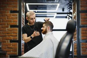Jeune Beau coiffeur fabrication la Coupe de cheveux de attrayant barbu homme dans salon de coiffure. photo