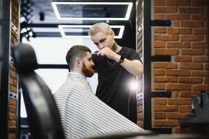 fabrication la Coupe de cheveux Regardez parfait. Jeune barbu homme avoir la Coupe de cheveux par coiffeur tandis que séance dans chaise à salon de coiffure. photo